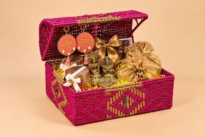 Pink cane basket Diwali hamper with Ganesh-Lakshmi idols, potli bags and festive treats, by Demould Delhi