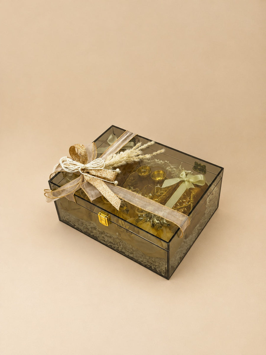 Premium smoked acrylic Diwali gift hamper with brass diyas, festive treats and gold ribbon bow for corporate gifting, by Delhi Gifting Company by Demould